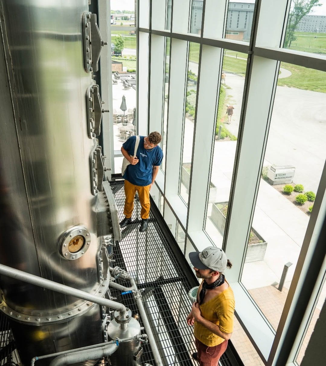 Bardstown Bourbon Company distillery interior with a team member inspecting stainless steel fermentation tanks.