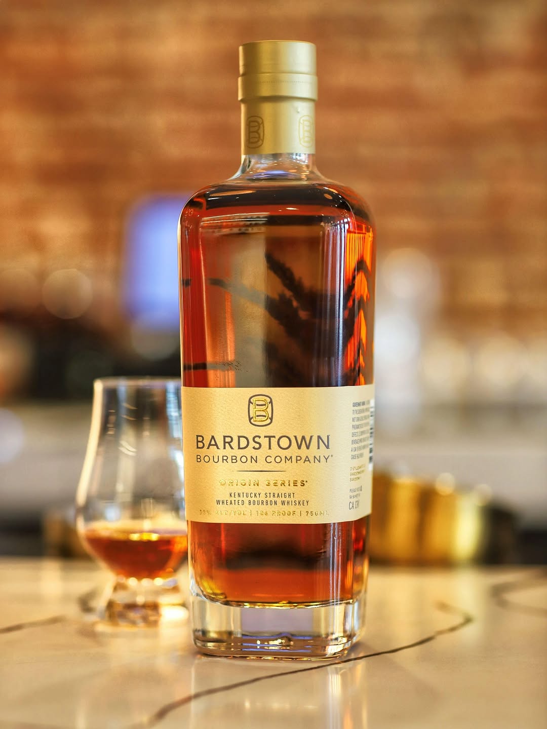 Bardstown Bourbon Company Origin Series bourbon bottle on bar with tasting glass, highlighting rich amber color.